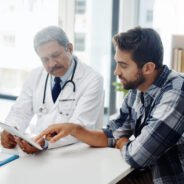 Healthcare, doctor and patient in consultation with tablet, expert advice, discussion and results. Medicine, health care and Indian man in doctors office, internet and consulting medical professional.