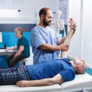 Chiropractor in blue scrubs uses osteopathic massage to help elderly male patient heal their hand muscles. Medical nurse helps old man extend his arm joint as part of his physical therapy.